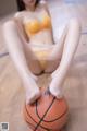 A woman in a yellow bikini sitting on a basketball.