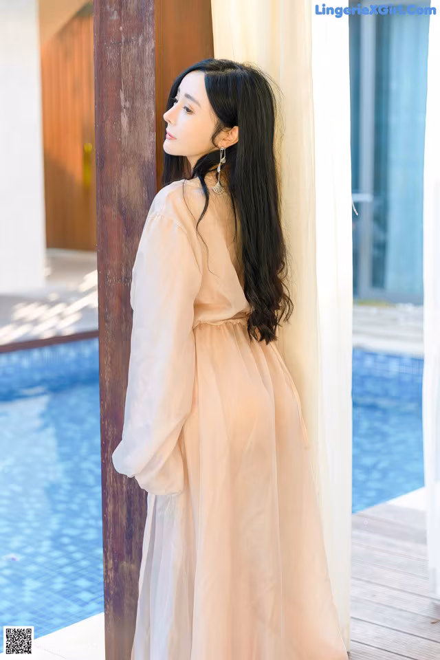 A woman leaning against a wall next to a pool.