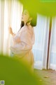 A woman in a white robe standing by a window.