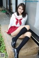 A woman in a school uniform sitting on a ledge.