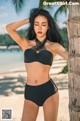 A woman in a black bikini standing next to a palm tree.