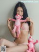 A woman sitting on a bed holding a pink stuffed animal.