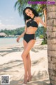 A woman in a black bikini standing next to a palm tree.