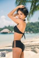 A woman in a black bikini standing on a beach.