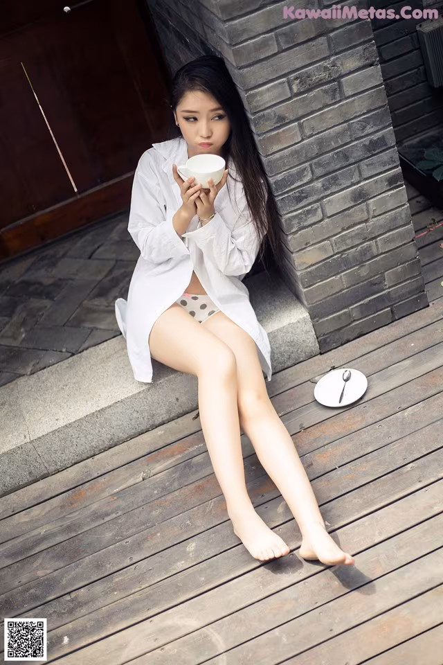 A woman sitting on a wooden floor holding a cup of coffee.