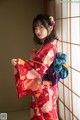 A woman in a red kimono standing in front of a window.