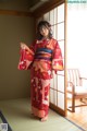 A woman in a red kimono standing in front of a window.