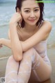 A woman in a white bodysuit sitting on the beach.