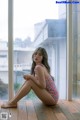 A woman sitting on a wooden floor in front of a window.