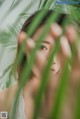 A woman in a white dress is looking through a palm tree.