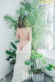 A woman in a white dress standing next to a plant.