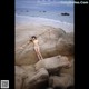 A woman in a yellow bikini sitting on a rock on the beach.