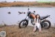 A woman sitting next to a motorcycle in a field.