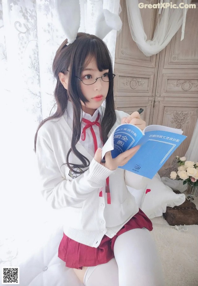 A woman in a white shirt and red skirt holding a book.