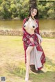 A woman in a red kimono posing next to a tree.