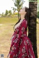 A woman in a red dress leaning against a palm tree.