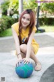 A young woman sitting on the ground with a basketball.