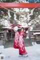 A woman in a red kimono holding a fan in the snow.